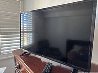 32-inch LG TV on wooden dresser with remote control placed in front, black frame and stand.