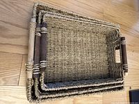 Three woven rectangular baskets nested inside each other showing size differences and design including wooden handles wrapped with rope.