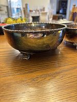 Close-up side view of one brass bowl showing beaded edge and claw feet, reflective surface with patina.