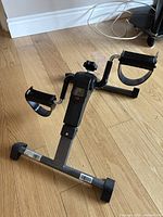 Stationary pedal exerciser shown from side angle highlighting pedals with straps and front display unit