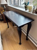 Long black wooden sofa table placed against a window wall, showing the full length and curved legs