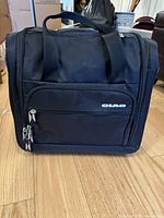 Front view of a black rectangular soft-sided CIAO carry-on bag with two front zipper pulls and two fabric carrying handles on top.