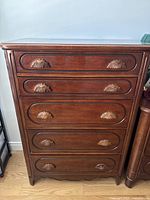 Front view showing five drawers with carved handles and decorative frame on a wooden dresser.