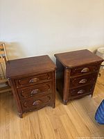 Front view of two matching antique solid oak nightstands with three drawers each, showing carved shell-style drawer pulls and wood grain finish.