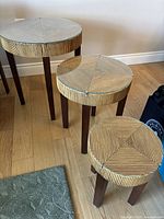 Photo showing three round stackable wood end tables with dark wood legs and striped wood top under glass, arranged side by side.