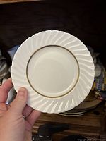 Front view of a white Royal Worcester fine bone china plate with twisted swirl rim and gold trim, held by hand.