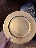 Single gold charger plate held in hand showing textured gold surface.