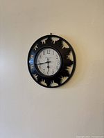 Round analog wall clock with black silhouette cutout frame shaped like city skyline detail hanging on wall.