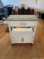 Front view showing granite top, drawer, open shelf, cabinet and casters