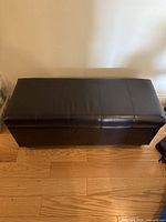 Top view of closed black faux leather storage bench showing stitched top surface and rectangular shape.