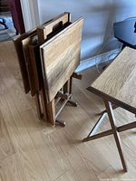 Four wooden TV table trays standing folded upright against a wall on wood floor