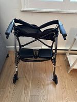 Front angle view of walker showing footrests, padded armrests, and storage basket underneath seat