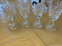 Front view of four Waterford crystal shot glasses showing the diamond-cut design and stemmed footed base on a gold cloth background.