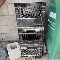 Stack of 3 black plastic milk crates with lattice sides, slightly dusty.