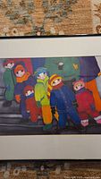 Framed art print showing colorful children in snowsuits, photographed on patterned carpet.