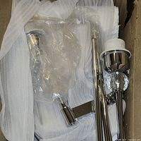 Chrome and crystal wall sconce parts wrapped in protective plastic and foam inside a box.