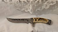 Knife with sharp blade displaying engraved design and carved handle featuring deer and fawn scene in relief.