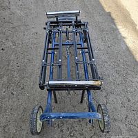 Top view of folded heavy duty miter saw stand showing frame, rollers, and wheels