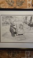 Framed grayscale print showing child with toy car and hose outdoors