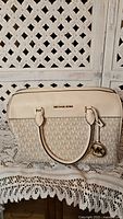 Front view of cream color Michael Kors handbag with MK monogram pattern and gold logo details.