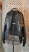 Black leather jacket with embroidered Team Canada 2002 gold medal championship maple leaf patch on chest, displayed on dress form.