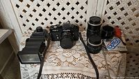 Overview of entire lot arranged on lace tablecloth showing camera, lenses, flash, filter and brush