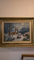 Full front view of the vintage needlepoint depicting a winter church scene in an ornate gold frame.