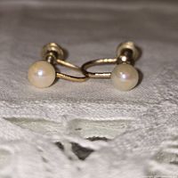 Close-up photo showing both vintage cultured pearl earrings with screw-back design, highlighting pearl luster and gold-tone metal.