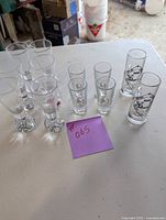 Front view of 12 shot glasses including tall, standard, and mug styles, with purple note #065 indicating lot number.
