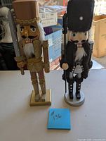 Two wooden nutcrackers: one brown with gold trim holding a sword, one black with tall fur hat holding a spear.