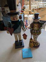 Two snowman nutcrackers standing side-by-side on a table with background items visible.