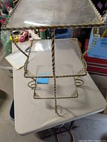 Front angled view of the 3 tier metal table showing the top and middle plexiglass shelves and twisted metal frame detailing.