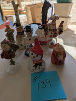 Eight snowman-themed bells arranged on a table showing varying shapes, colors, and heights from 3 to 7 inches.