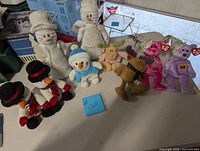 Wide view showing all 9 plush toys together on table including snowmen, moose, and bears