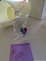 Front view of clear crystal bunny perched upright holding a basket with colorful crystal eggs inside.