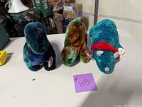 Three dinosaur Beanie Babies displayed on a table, showing front view with tags.