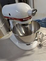 Side view of white KitchenAid Classic mixer with attached stainless steel bowl and whisk attachment beside it.