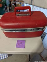 Closed small red makeup suitcase with handle and silver trim sitting on a table.