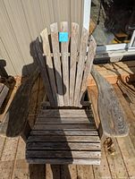Front view of the wooden Muskoka chair showing the fan-shaped backrest with five vertical wooden slats, wide curved armrests, and slatted seat. Wood has a weathered appearance but no visible rot.