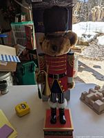 Front view of wooden bear nutcracker dressed in red soldier uniform, standing on a red base, 25 inches high.