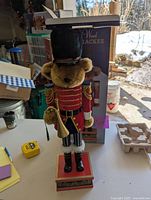 Front view of wooden bear nutcracker standing on table with its box behind it.