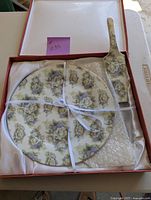 Porcelain cake plate and cake server set in original box tied with white ribbon. Floral design in white, green, and beige on porcelain.
