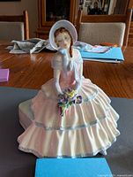Front view of Royal Doulton figurine "Daydreams" showing the seated young woman in bonnet and pastel pink dress holding flowers.