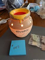 Front view of the Hunny pot wax warmer lit to show glowing warm light, yellow honey dripping from top rim, 'Hunny' written on front