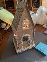 Front angled view of the ceramic gingerbread house wax warmer with lighted windows and candy details on front.