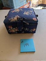 Blue floral fabric-covered sewing box on a surface with a blue sticky note marked #144.