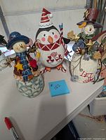 Front view of two snowman figurines and metal penguin figurine on a table.