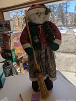 Full frontal view of the fabric snowman greeter showing entire body, clothing details, and broom in hand.