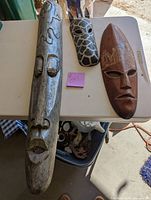Photo of three wooden masks of different sizes and colors placed on a white table showing their scale and design details.