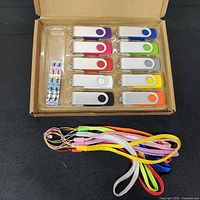 Photo of 10 USB thumb drives in various colors arranged in a box, showing metallic swivel covers.